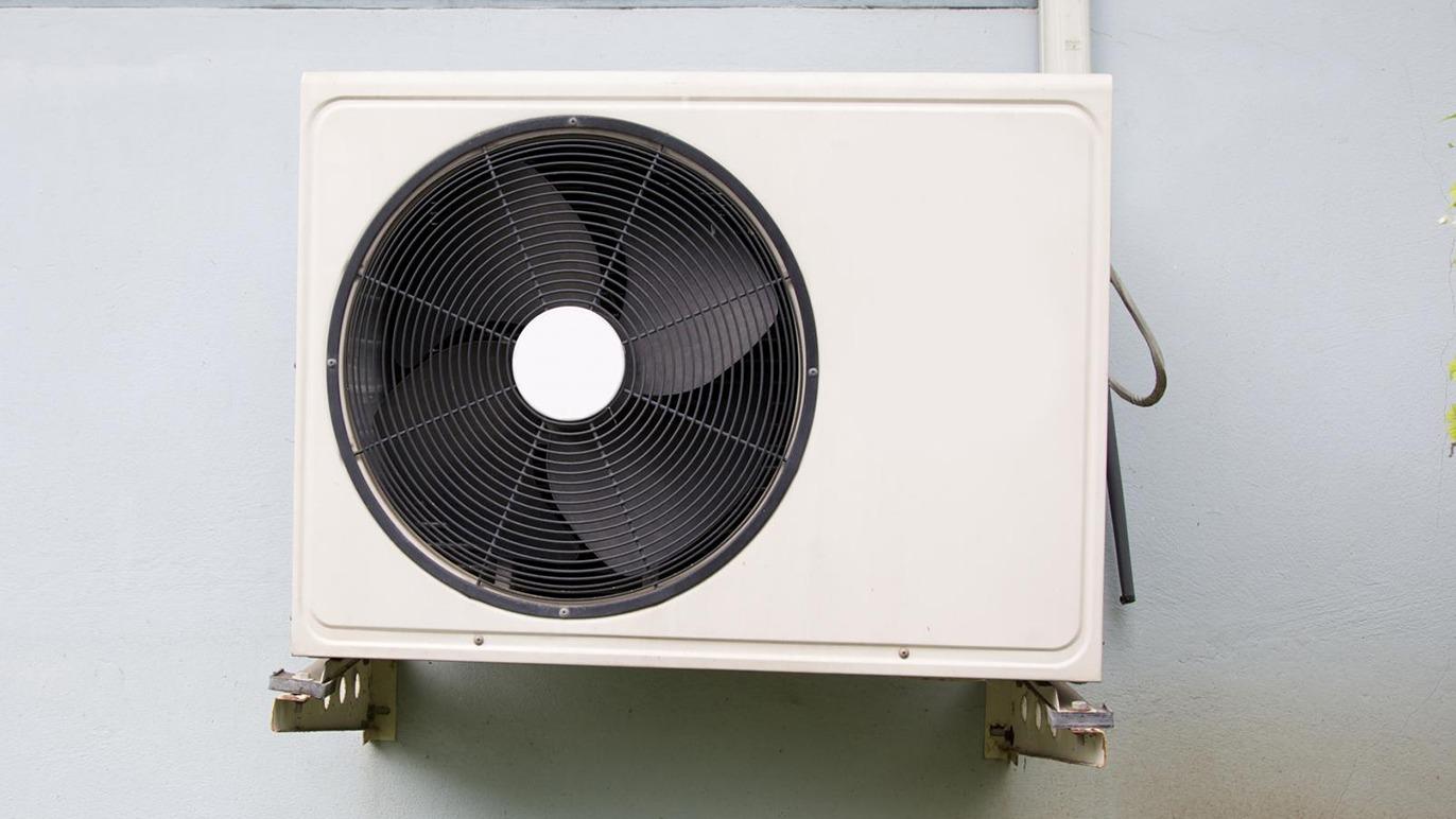 Udendørs klimaanlæg monteret på væg med sort ventilator og hvidt kabinet.