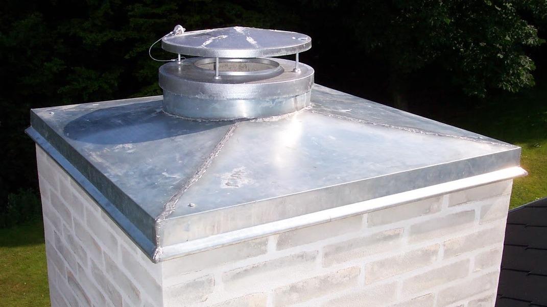 Metal skorsten med ventilationshætter på toppen, placeret på en murstensbygning.
