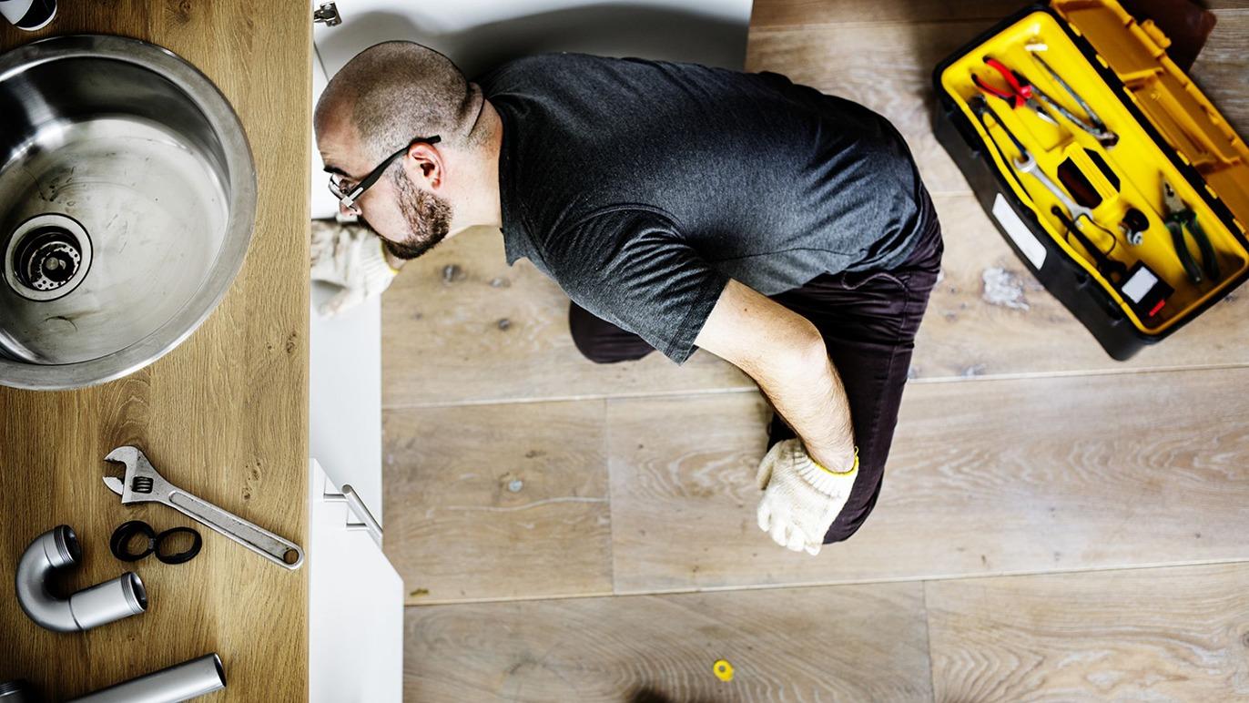 En mand arbejder under en vask med værktøjskasse ved siden af, mens han reparerer rør.