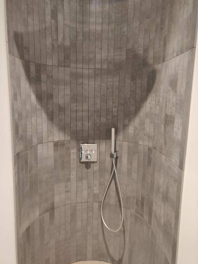 Bruser med grå fliser og moderne armatur på væggen, der skaber en minimalistisk og stilren atmosfære.