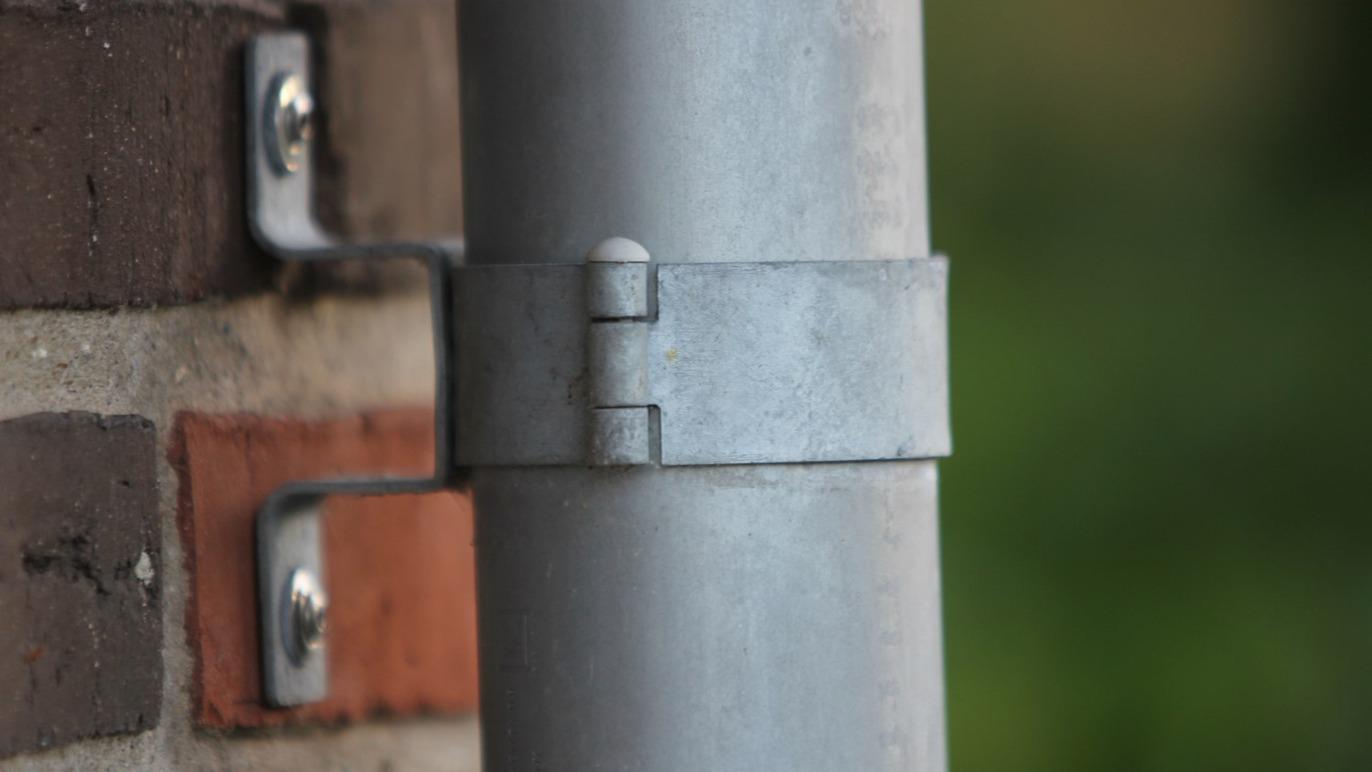 Nærbillede af en metalrørbeslag, der holder et rør fast til en mur.