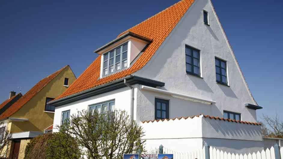 Et hvidt hus med rød tag og blå vinduer under en klar blå himmel.