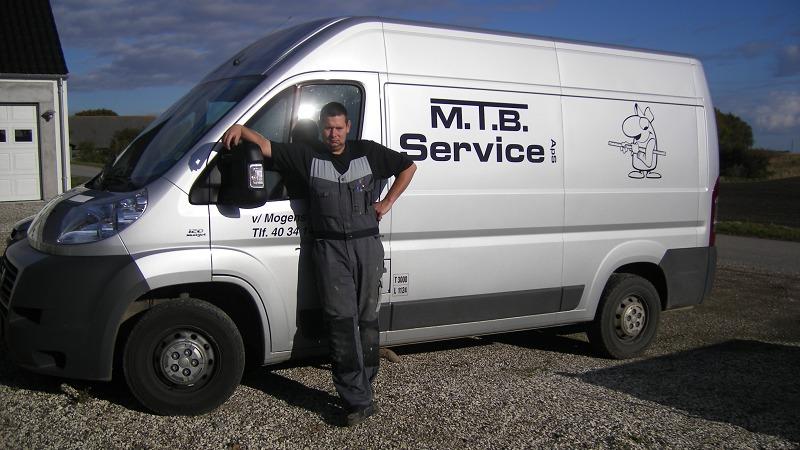 En mand står ved siden af en hvid servicevogn med teksten "M.I.B. Service" på siden.