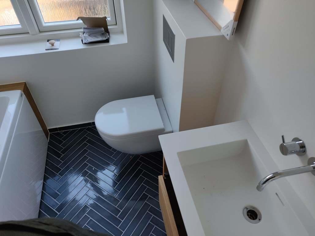 Moderne badeværelse med hvid toilet, håndvask og mørke fliser i zigzag mønster.
