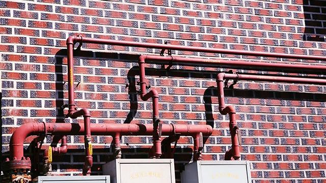 Rørinstallationer i rød farve på en murstensvæg med elektriske målere nedenfor.