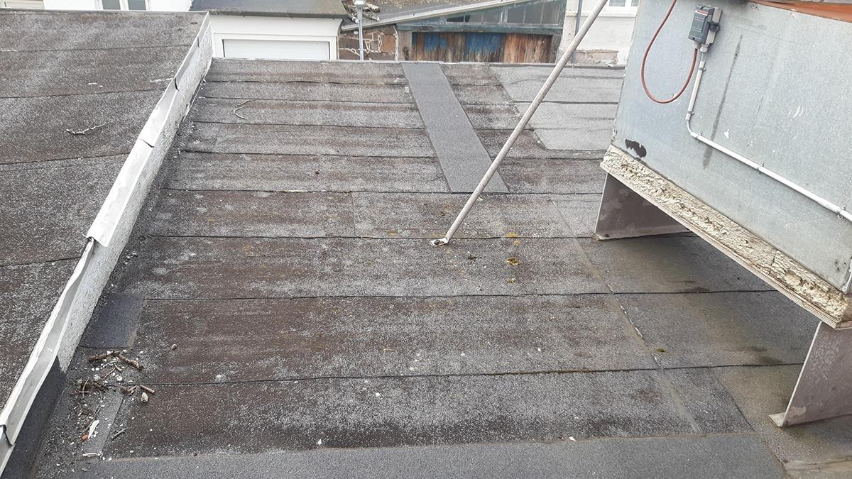 Tag med slidte tagplader og en ventilationskanal på en bygning.