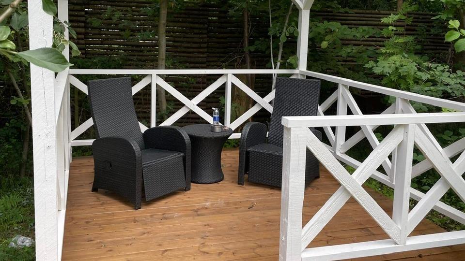 To sorthvide havemøbler i en pavillon med et lille bord og grønne planter i baggrunden.