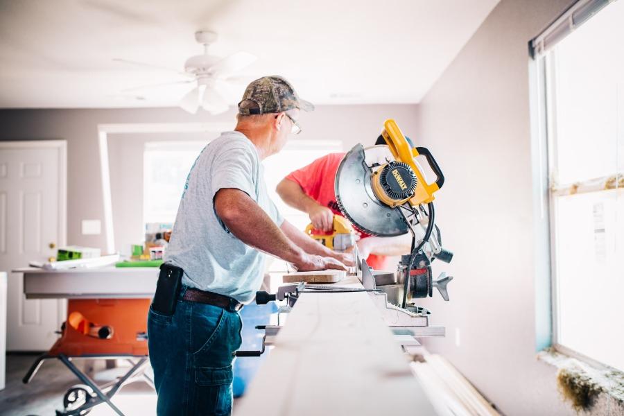 To håndværkere arbejder sammen med en rundsav i et lyst rum under renovering.