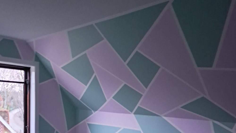 Væg med geometriske mønstre i pastelfarver som grøn, lyserød og hvid i et værelse.