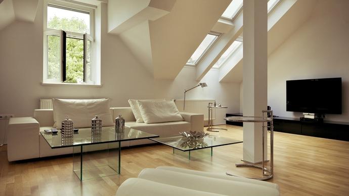 Moderne stue med hvid sofa, glasbord og store vinduer, der giver naturligt lys.