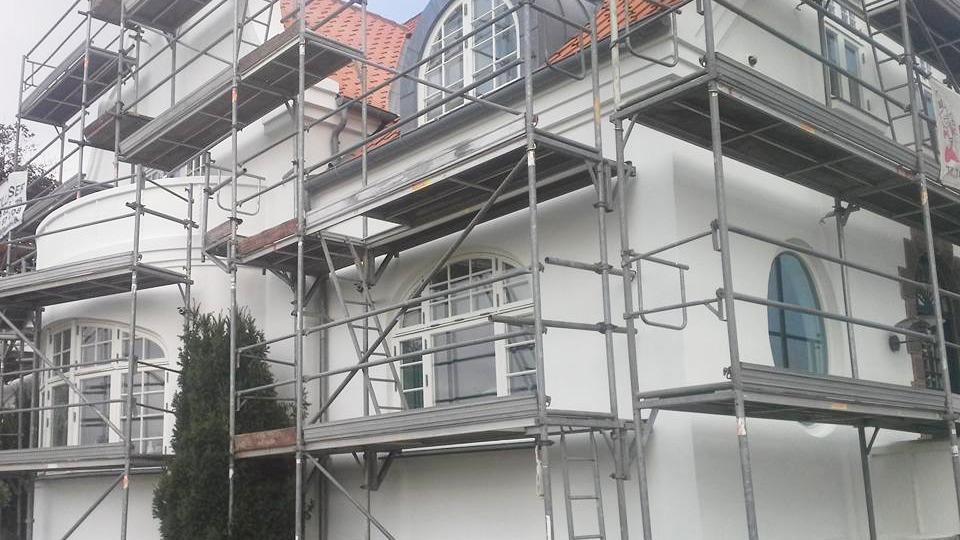 Hus under renovering med stillads og hvid facade, der viser detaljer som vinduer og tag.