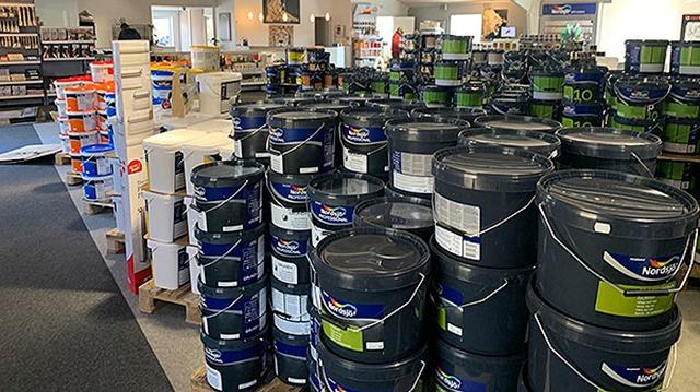 Butik med malerbøtter i forskellige størrelser og farver, organiseret på hylder og palleplader.