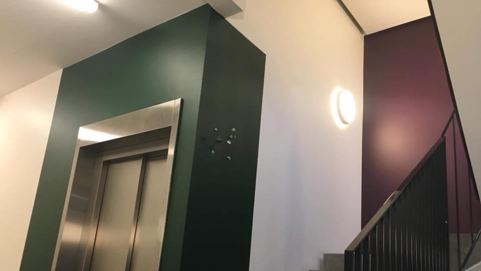 Indgang til en moderne elevator i en bygning med grøn og lilla vægfarve. Trappeopgang synlig til venstre.