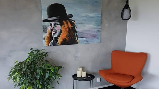 Et moderne rum med en orange stol, et maleri af en klovn og en grøn plante ved siden af et lille bord med lys.