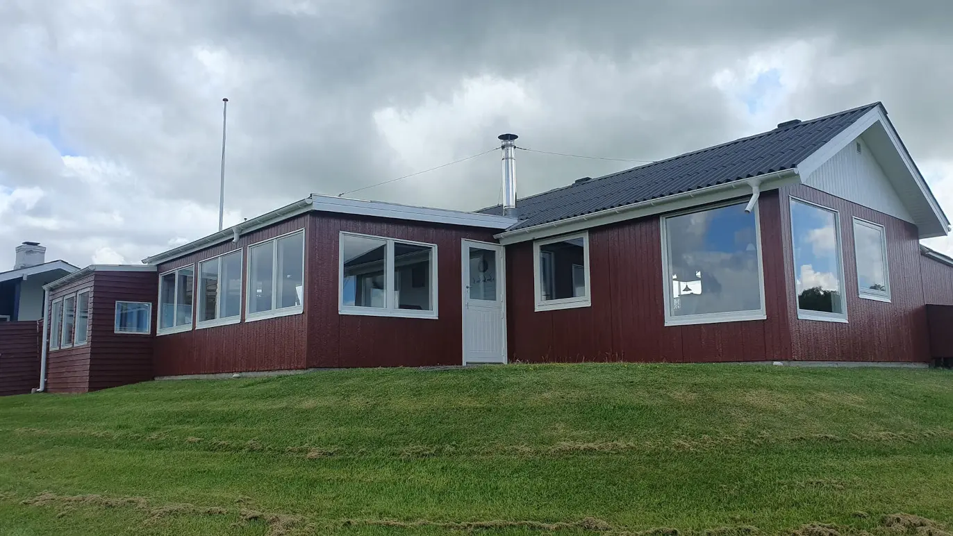 Rødt hus med mange vinduer og græsplæne under en skyet himmel.
