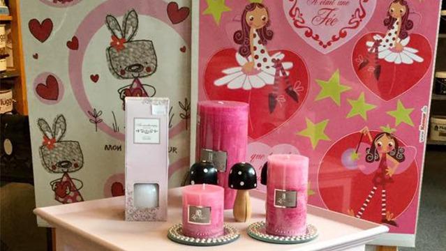 Dekorativt bord med lyserøde stearinlys, en parfume og farverige figurer på baggrunden.