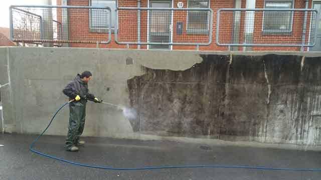 En mand, der højtryksrenser en beskidt væg i et bymiljø.