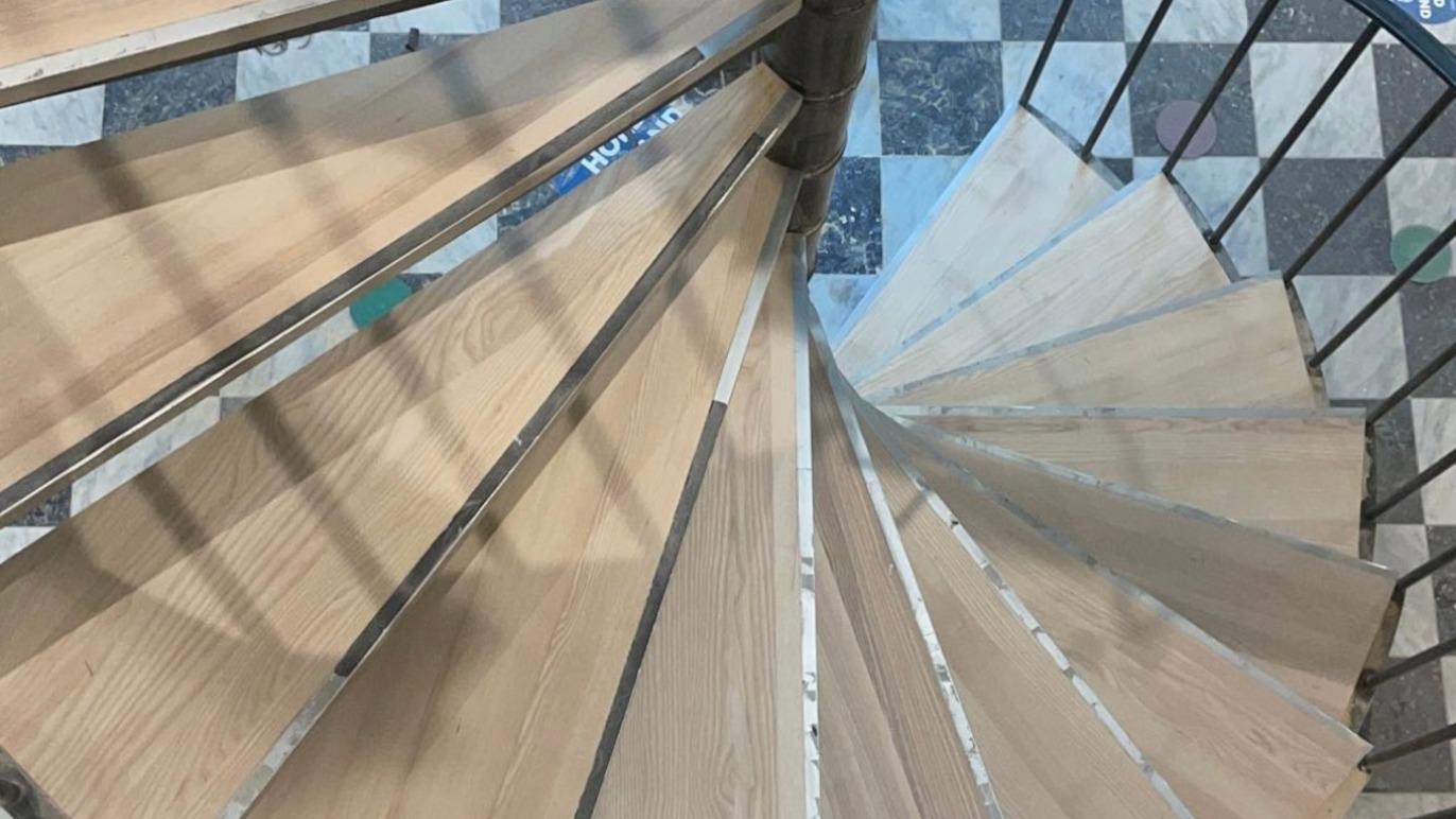 En spiraltrappe med trætrin og metalgelænder set oppefra, der viser en geometrisk mønster.
