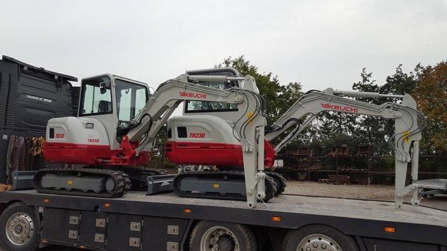 To storede gravemaskiner på en lastbil, klar til transport, med rød og hvid farve.