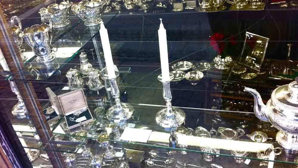 Sølvlysestager og tepotte i en udstillingsvitrine med forskellige sølvgenstande.