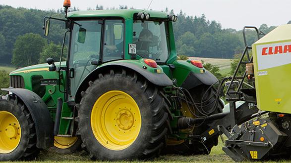 Traktor med gule dæk og en grøn maskine til høstning på en mark i landskabet.