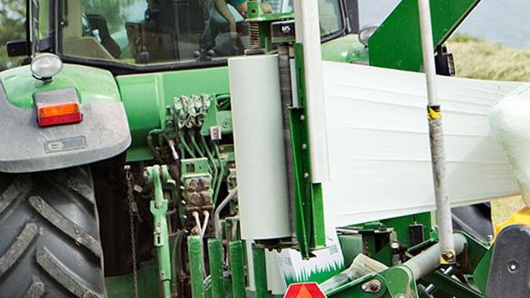 Traktor med grønne detaljer og udstyr til høst, der viser hydrauliske systemer og rulle til indpakning.