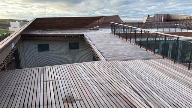 Udsigt over en træterrasse med moderne bygninger og himmel i baggrunden.