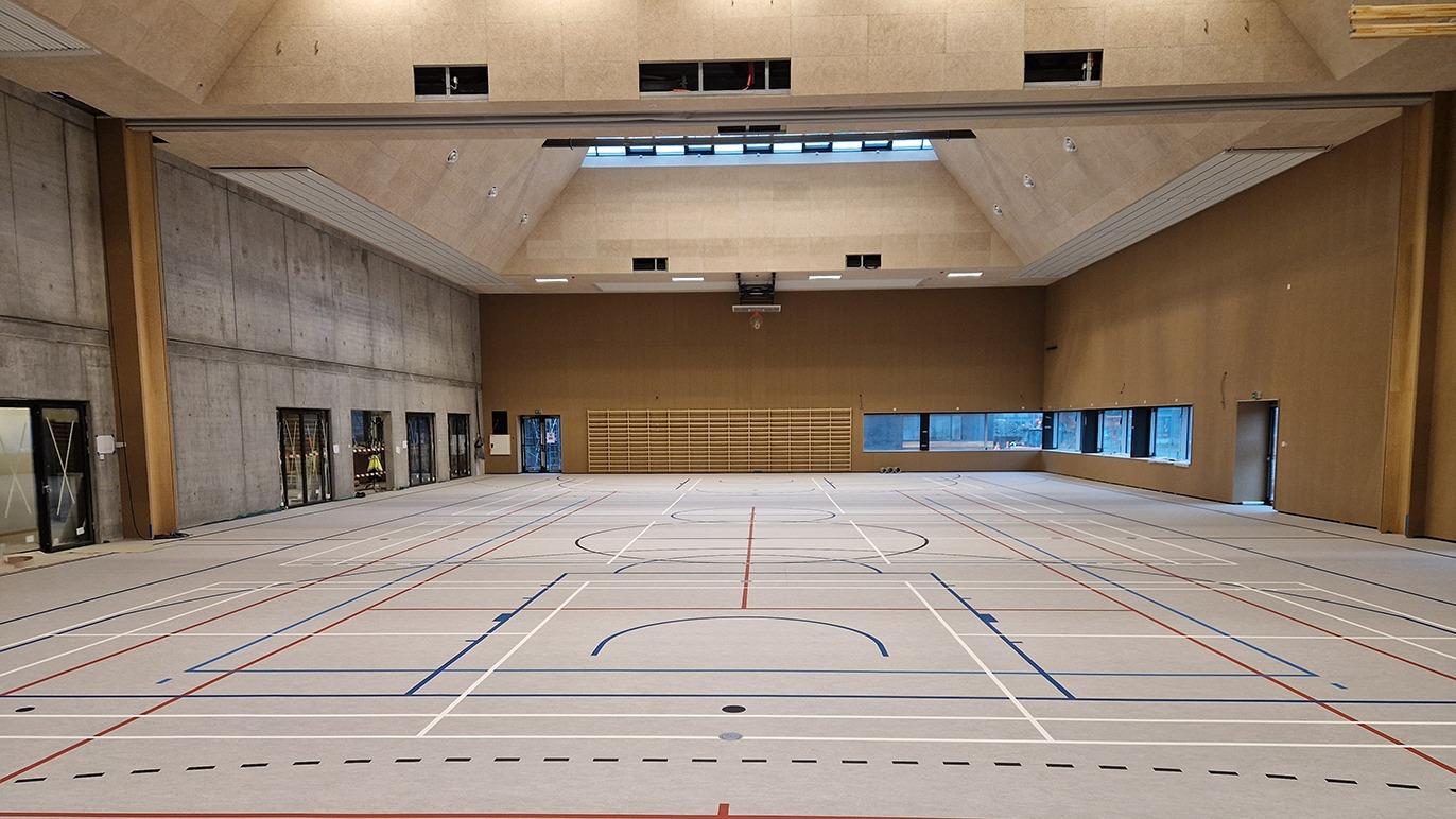 Indendørs sportshal med en stor, tom bane og synlige linjer til forskellige sportsgrene.
