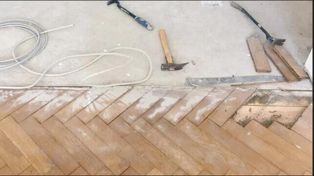 Billede af et gulv med parketbrædder, værktøj og ledninger til renovering af et rum.