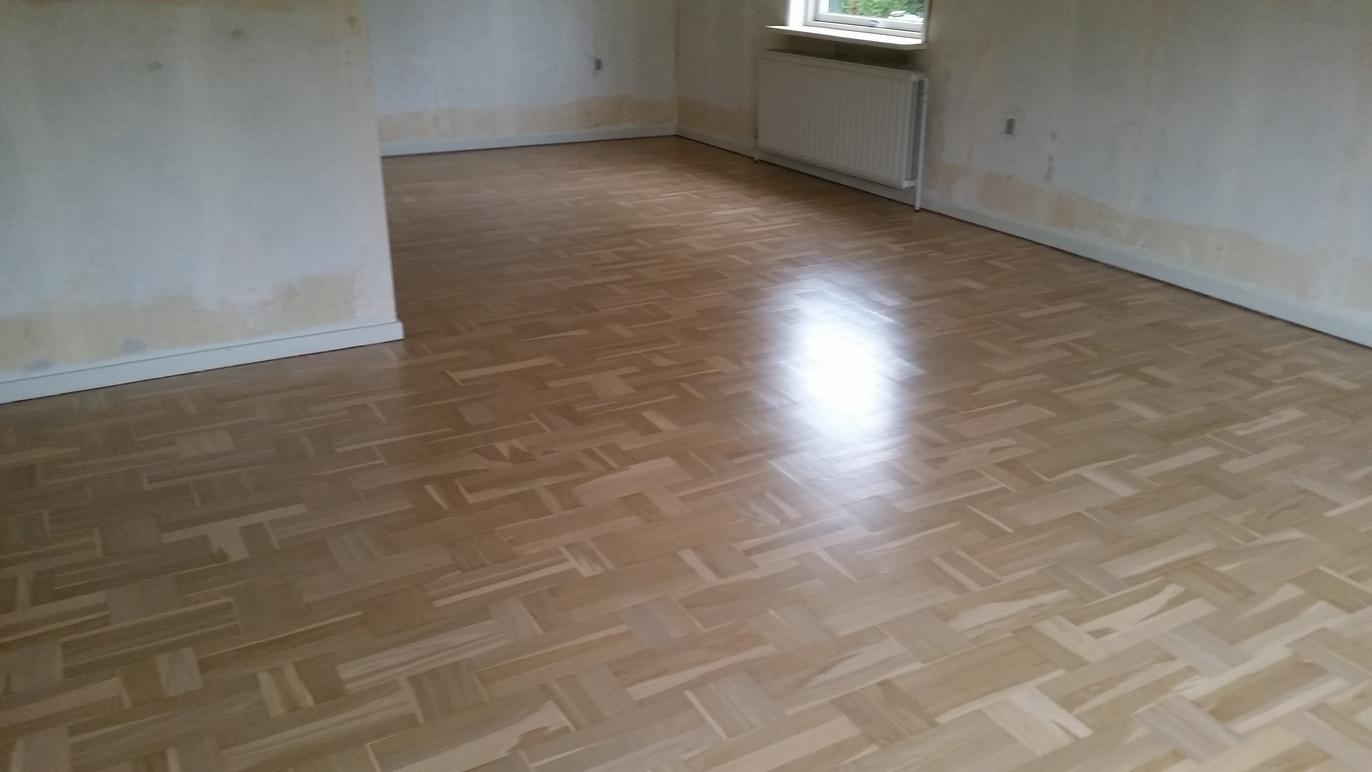 Et tomt rum med lyst parketgulv og vægge, der er delvist malet i beige.