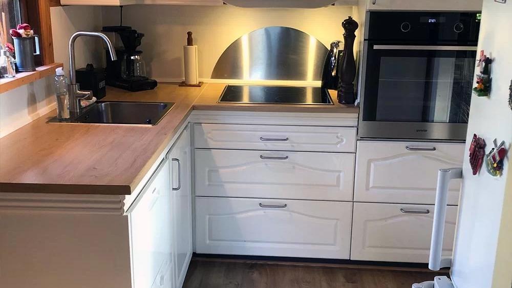Moderne køkken med hvidt skab, træbordplade, komfur, vask og kaffemaskine. God belysning og stilrent design.