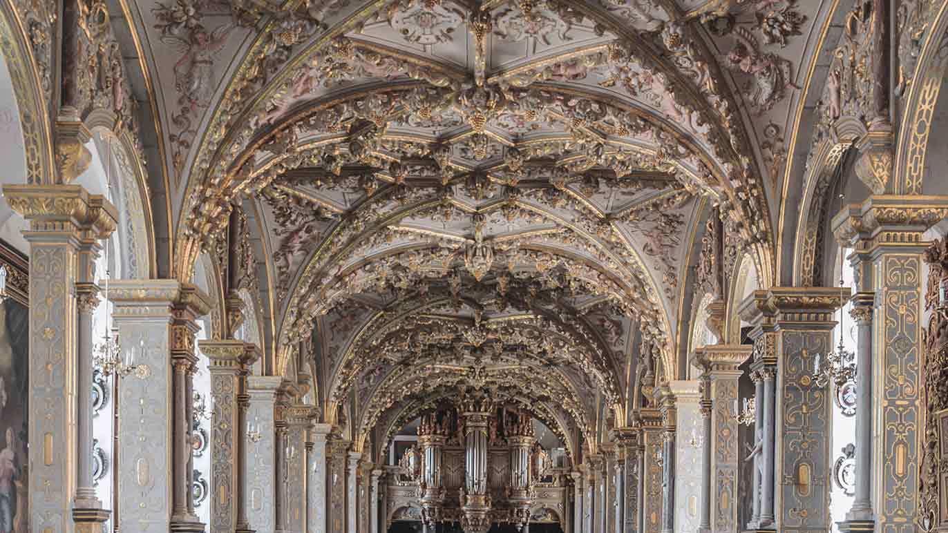 Et overdådigt rum med udsmykkede lofter og søjler, prydet med detaljeret kunst og ornamenter.