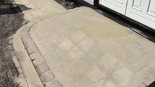 Nybelagt indkørsel med brosten og glat overflade foran en hvid dør.