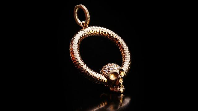 Guldhalskæde med en skalleformet vedhæng og en slangeformet ring, dekoreret med diamanter.