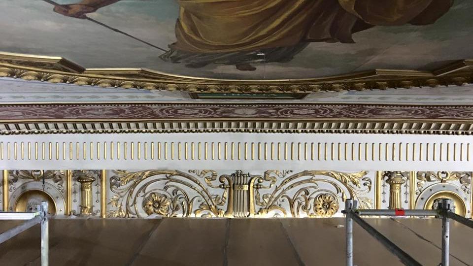 Detalje af en udsmykket loft med malerier og gyldne dekorationer i en historisk bygning.