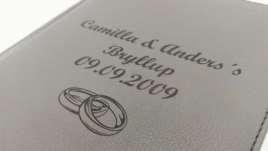 Bryllupsalbum med navne og dato, samt indgraverede vielsesringe på forsiden.