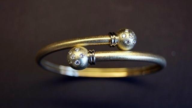 Et elegant armbånd i guld med to dekorative kugler i enderne.