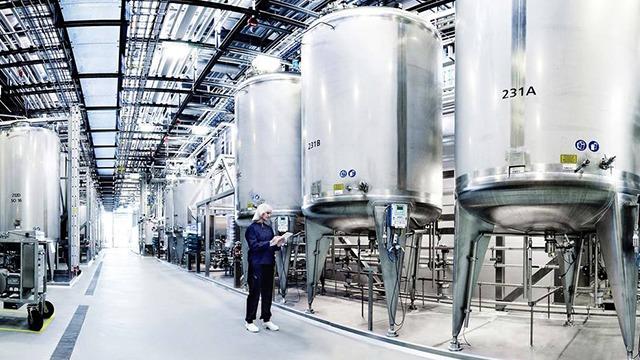 En medarbejder står ved store metalbeholdere i en moderne produktionshal med højt til loftet.