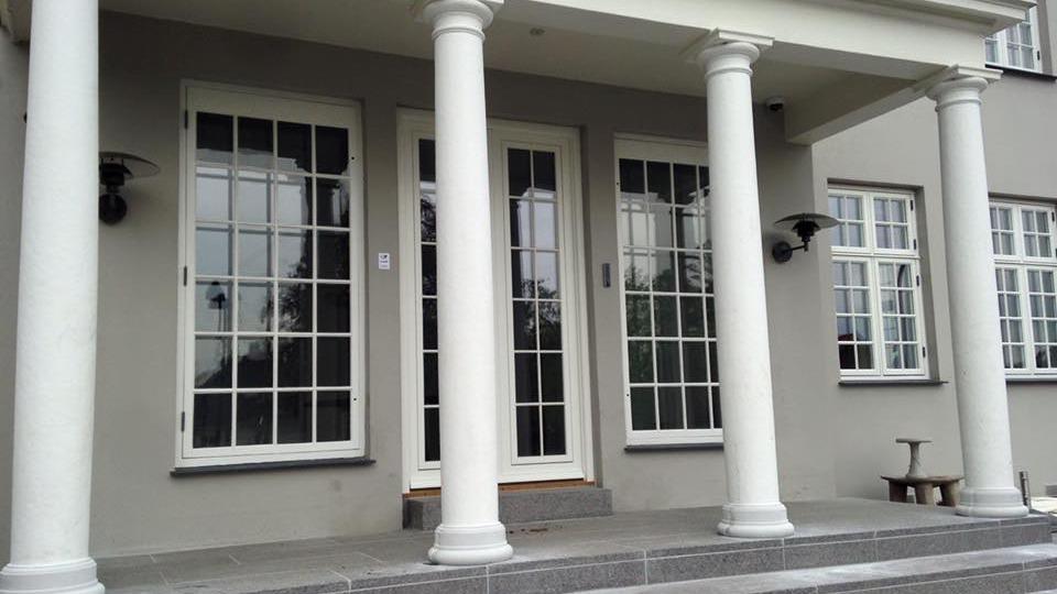 Facade af et hus med søjler, store vinduer og en dør, der fører ind til bygningen.