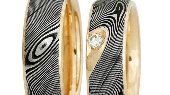 To ringe i guld og sort med bølgemønster og en diamant i den ene ring. Elegant og moderne design.
