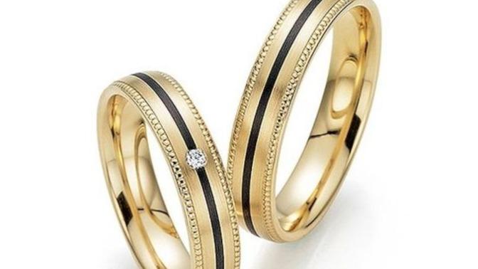 To smukke guld vielsesringe med sorte striber og en diamant på den ene ring.
