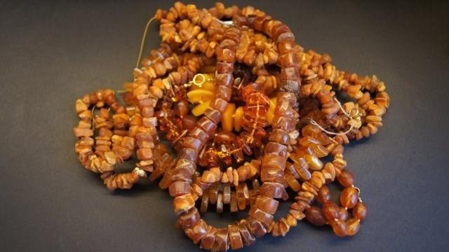 En samling af brune ravperler i forskellige former og størrelser, der ligger sammenfiltret på en mørk baggrund.