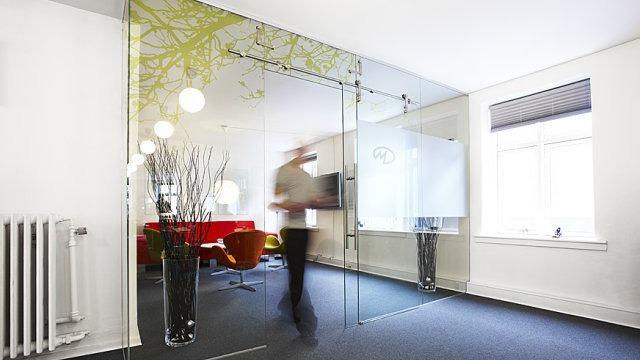 En moderne kontorindretning med glasvægge, planter og en person, der går forbi.