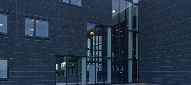 Moderne bygning med mørke facader og store glaspartier ved indgangen.