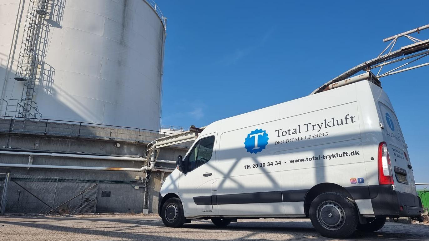 Total Tryklufts varevogn parkeret ved en stor tank under en klar blå himmel.