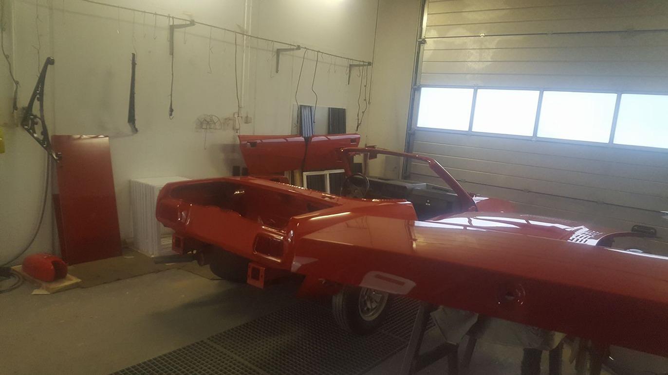 Rød bil i en garage med værktøj og udstyr på væggene.
