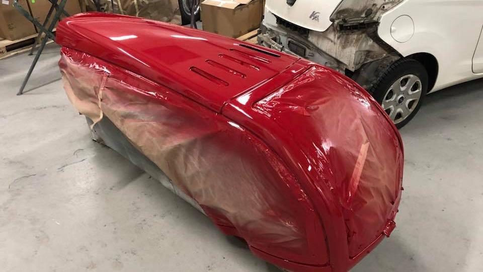 Rød bilkarrosseri dækket med plast i et værksted, klar til malerarbejde.