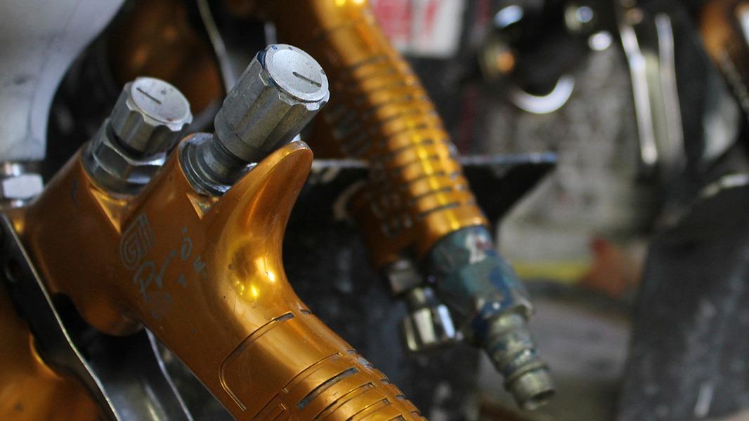 Nærbillede af orange motorcykelkomponenter med metalventiler og slanger i et mekanisk værksted.