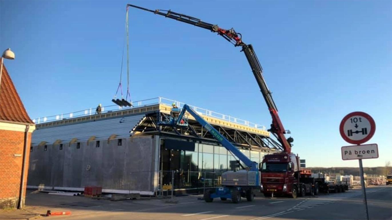 Byggeri af en moderne bygning med kran og stillads under solskin.