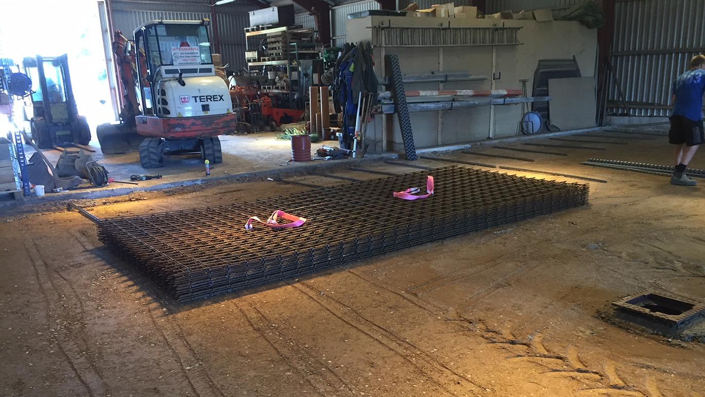 Billede af en stor metalramme på gulvet i en lagerhal med værktøj og maskiner i baggrunden.